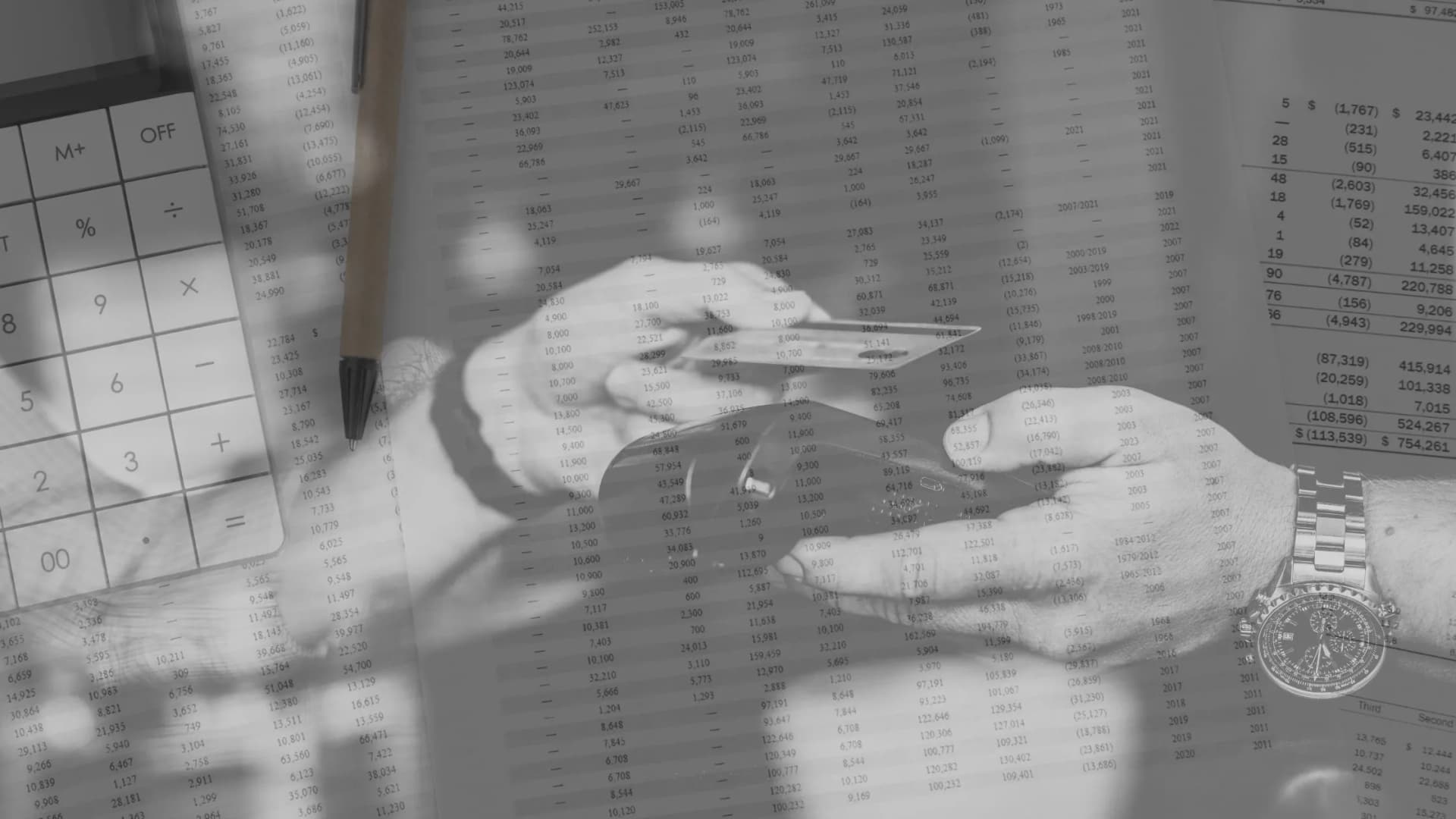 Hands holding a credit card with financial documents and a calculator in the background, representing the Visa and Mastercard settlement and its effects on merchants.